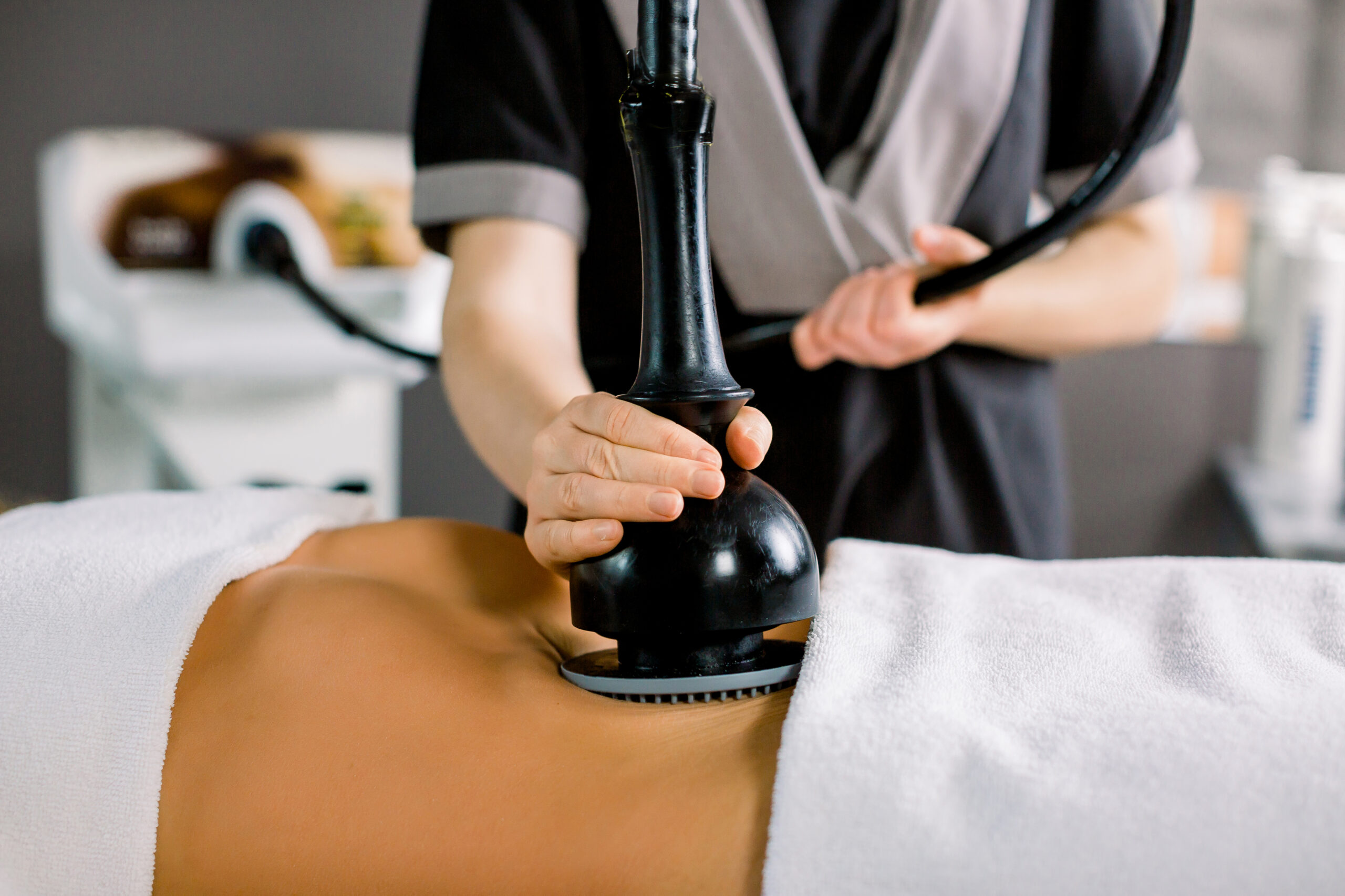 Vacuum massage device, anti cellulite body correction. Cropped image of woman client receiving vacuum massage of the abdomen and hands of female doctor holding the device.